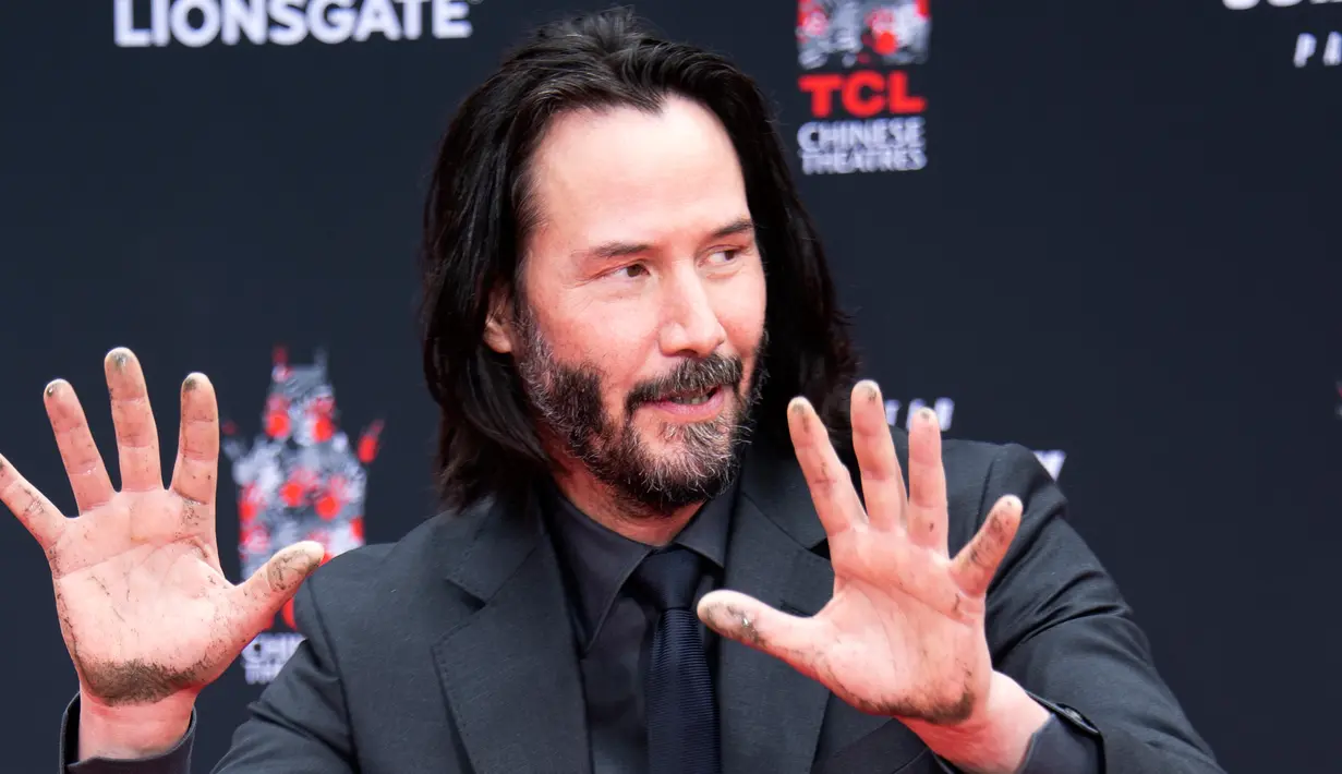 Aktor Keanu Reeves menunjukkan telapak tangannya yang masih berlumuran semen di halaman depan TCL Chinese Theatre, Los Angeles, Selasa (14/5/2019). Aktor 54 tahun itu mendapat penghargaan membuat cetakan tangan dan kaki untuk merayakan keberhasilan karirnya dalam film. (VALERIE MACON / AFP)