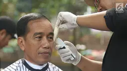 Presiden Joko Widodo saat mengikuti acara cukur ram but missal di Garut, Jawa Barat, Sabtu (19/1). Tak hanya Jokowi, Menteri PUPR Basuki Hadimuljono serta Kepala Sekretariat Presiden Heru Budi Hartono  ikut memangkas rambutnya. (Liputan6.com/Angga Yuniar)