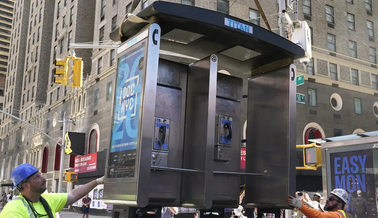 Para pekerja memindahkan bilik telepon umum terakhir NYC di dekat Seventh Avenue dan 50th Street di Midtown Manhattan, New York City, pada 23 Mei 2022. Telepon umum mulai menghilang dari jalan-jalan di New York pada awal 2000-an saat penggunaan telepon selular menyebar, dan kemudian menghilang lebih cepat pada 2010-an saat terjadi booming telepon pintar. (TIMOTHY A. CLARY / AFP)