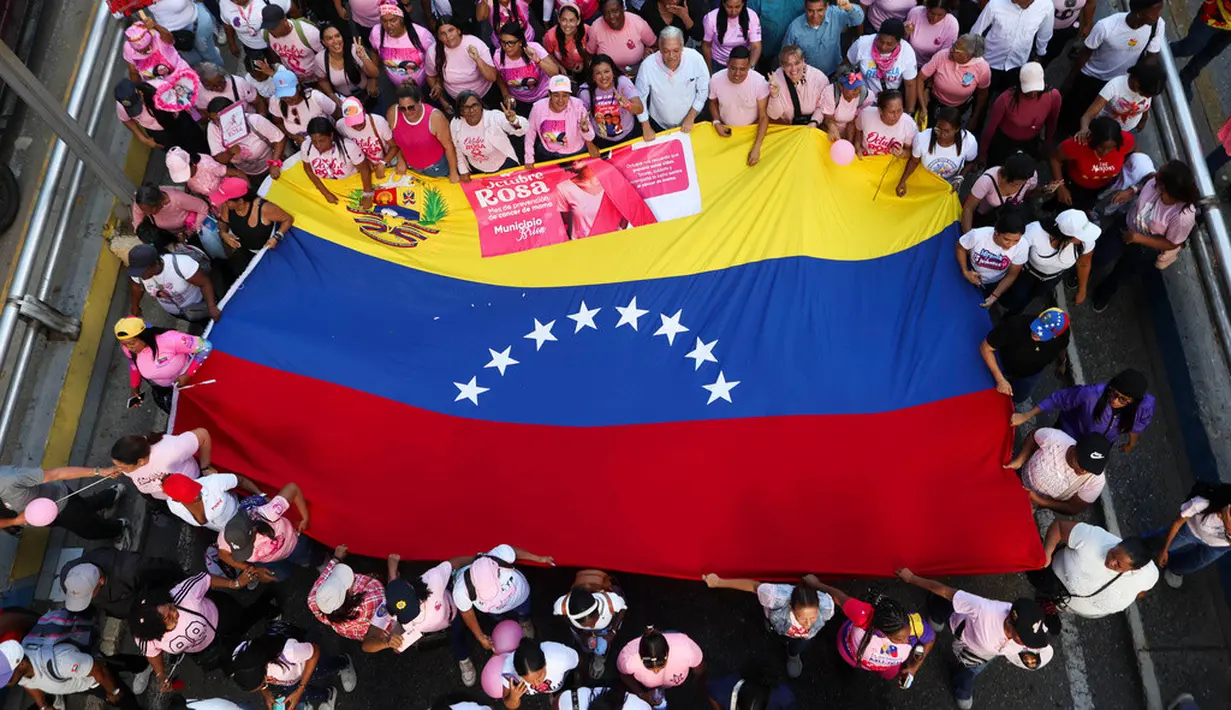 Sejumlah warga mengibarkan bendera nasional Venezuela saat mengikuti pawai yang diselenggarakan pemerintah untuk meningkatkan kesadaran terhadap kanker payudara dalam rangka Bulan Peduli Kanker Payudara atau Pink Month di Caracas, Venezuela, Kamis (22/10/2026). (AP Photo/Pedro Mattey)