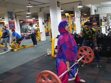 Seorang wanita Muslim India mengangkat beban saat berlatih di gym Ahmedabad Fitness Academy (AFA) di Ahmedabad (10/5/2019). Selama bulan suci Ramadhan, tempat gym ini tetap buka hingga larut malam untuk membiarkan anggota Muslim berolahraga setelah salat. (AFP Photo/Sam Panthaky)