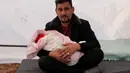 Khalil al-Suwadi menggendong keponakannya Afraa, bayi Suriah yang lahir di bawah reruntuhan setelah gempa bumi 6 Februari yang melanda Turki dan Suriah yang menewaskan orang tua dan saudara kandungnya, di kota Jindayris yang dikuasai pemberontak di Suriah utara, Selasa (21/2/2023). Bayi itu, terbungkus selimut dan mengenakan topi merah dengan pita kecil, diberi nama ibunya, Afraa - salah satu dari lebih dari 45.000 orang yang tewas di Suriah akibat gempa bermagnitudo 7,8.  (Rami al SAYED / AFP)