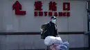 Seorang pelancong yang mengenakan masker untuk melindungi dari penyebaran virus corona membawa barang bawaannya di Stasiun Kereta Api Beijing di Beijing, Kamis (28/1/2021).  (AP Photo/Mark Schiefelbein)