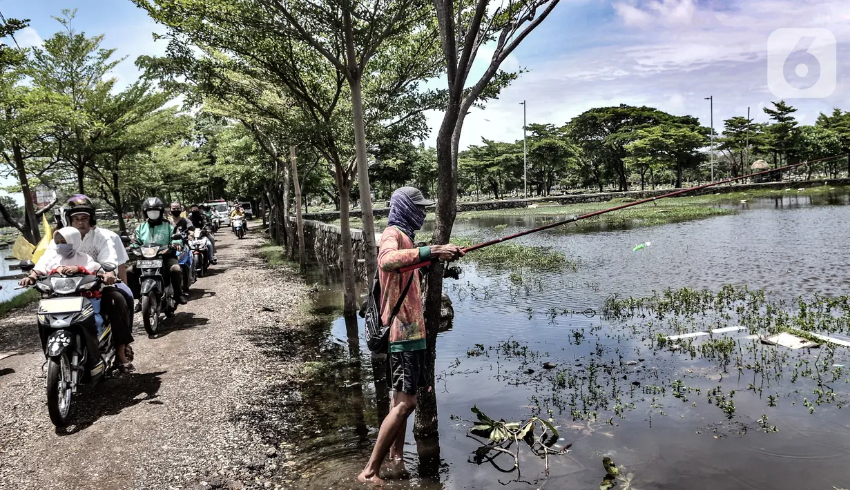 Rombongan pengantar jenazah melintas di dekat Amir yang tengah memancing di TPU Semper, Jakarta, Selasa (2/2/2021). Banjir tersebut dimanfaatkan warga setempat untuk mencari ikan dengan menggunakan alat pancing serta jala. (merdeka.com/Iqbal S. Nugroho)