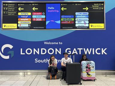 Para penumpang duduk di depan papan informasi yang menunjukkan lokasi meja maskapai di Bandara Gatwick dekat London, Inggris, Kamis 12 Juni 2025. (AP/Kin Cheung)
