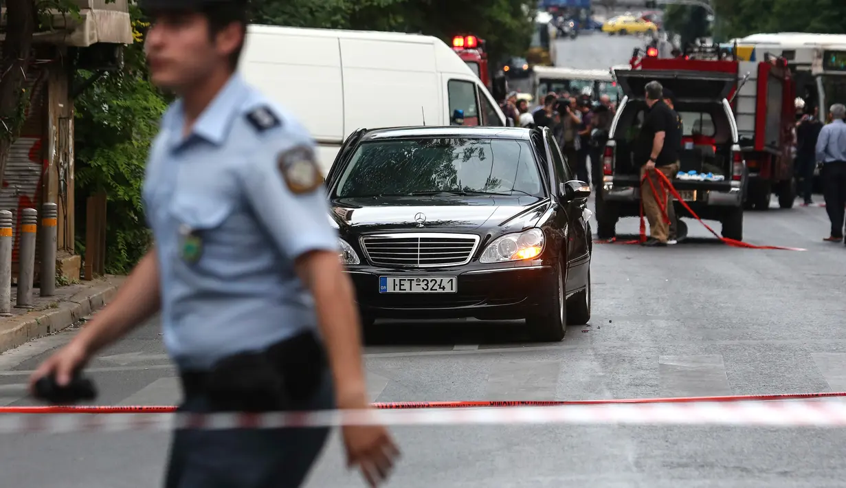 Seorang polisi berjalan dekat sebuah mobil di lokasi ledakan di pusat kota Athena, Kamis (25/5). Mantan PM Yunani, Lucas Papademos mengalami luka bakar di kaki dan tangannya akibat sebuah paket meledak di dalam mobil tersebut. (AP Photo/Yorgos Karahalis)