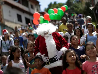 Santa Claus berjalan bersama kerumunan anak-anak di kawasan kumuh Petare di Caracas, Venezuela (11/12). Petare adalah sebuah kawasan yang masuk dalam ibukota Caracas dan terkenal kumuh. (Reuters/Ueslei Marcelino)