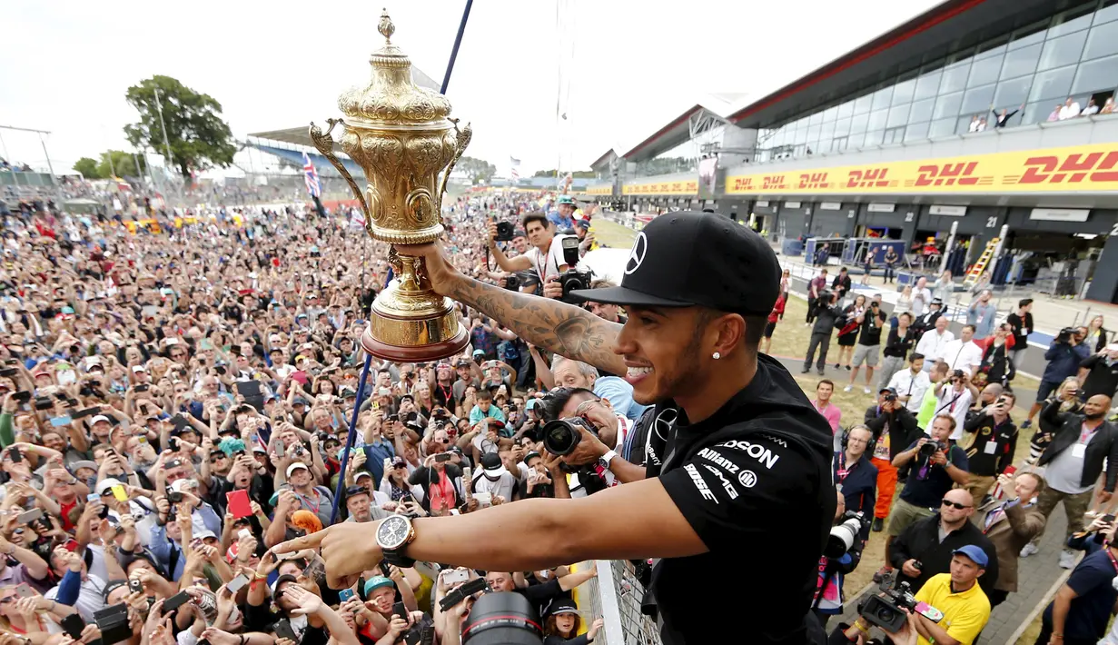 Pembalap Formula 1, Lewis Hamilton menunjukan trofi  ke pengemarnya usai berlaga di Grand Prix Formula 1 Silverstone di Inggris, (5/7/2015). Hamilton berhasil finish di urutan pertama dengan waktu 1 jam 31 menit 27,729 detik. (Reuters/Hoch Zwei)