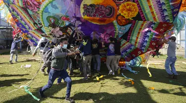Warga membantu mengangkat layang-layang raksasa untuk ditampilkan pada Hari Semua Orang Kudus sebagai bagian dari perayaan Hari Kematian di Santiago Sacatepequez, Guatemala, 1 November 2021. Perayaan digelar dengan sejumlah pembatasan untuk mengekang penyebaran COVID-19. (AP Photo/Moises Castillo)