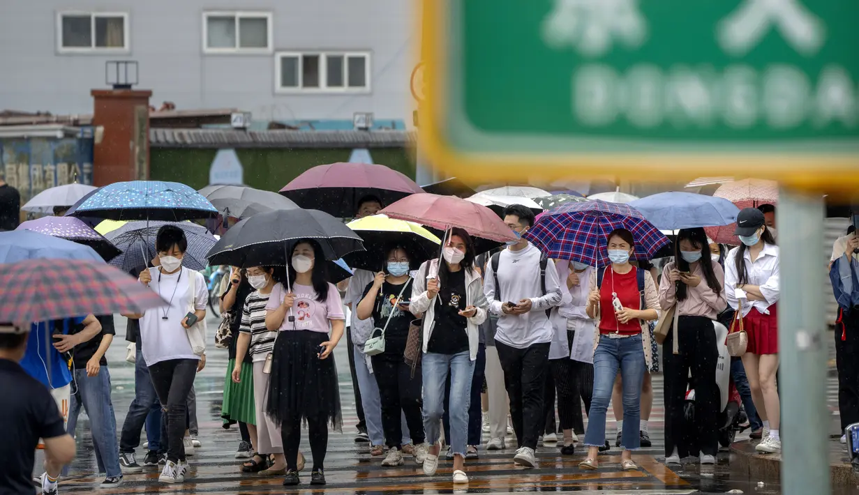 Para komuter yang mengenakan masker berjalan melintasi penyeberangan selama jam sibuk pagi hari pada hari hujan di Beijing, Rabu (29/6/2022). China pada hari Selasa memutuskan untuk memangkas setengah waktu karantina bagi pelancong yang masuk ke Negara Tirai Bambu itu.  (AP Photo/Mark Schiefelbein)