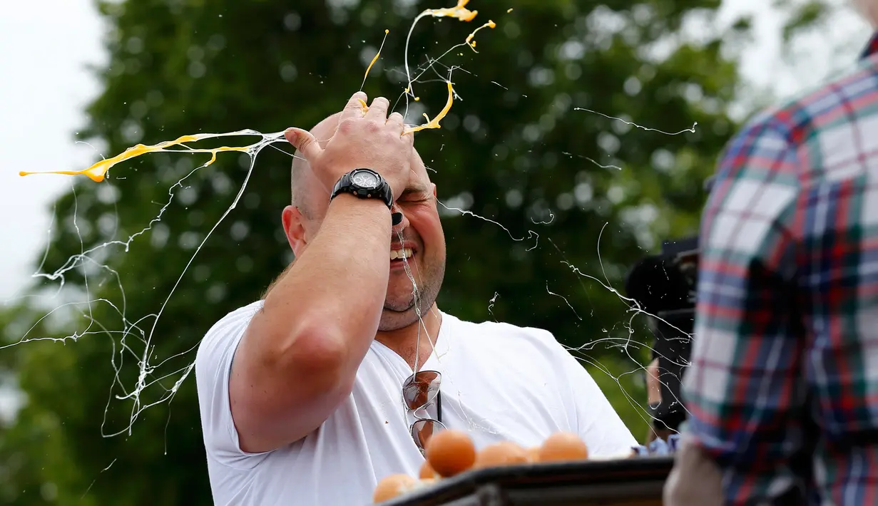 Seorang pria memecahkan telur dikepalanya usai kalah dalam permainan Russian Egg Roulette pada acara Kompetisi Melempar Telur Dunia dan Vintage Day di Swaton, Inggris, Minggu (28/6/2015). (REUTERS/Darren Staples)