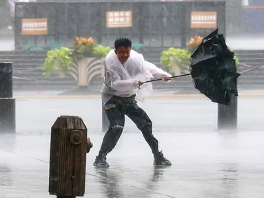 Seorang pria berjuang mempertahankan payungnya di tengah angin kencang dan hujan menjelang kedatangan Topan Dolphin di Distrik Huangpu, Shanghai, Tiongkok, Minggu, 9 Agustus 2026. (Xinhua via AP/ Wang Xiang)