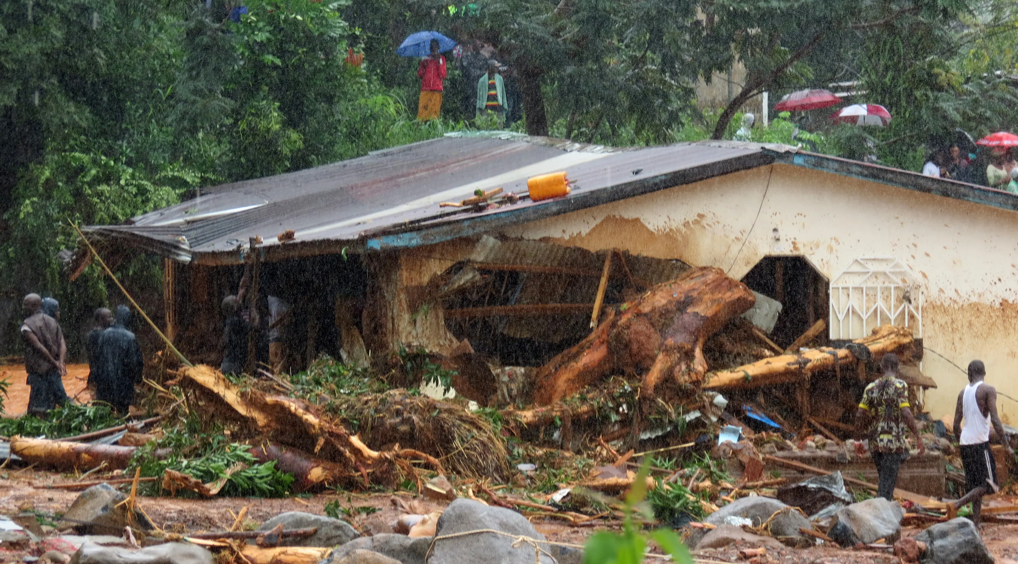 Petugas dibantu warga melakukan pencarian korban usai tanah longsor di Regent, Freetown, Sierra Leone, (14/8). Bencana ini terjadi saat penduduk tengah tidur sehingga banyak yang terjebak di dalam rumah. (AFP Photo/Saidu Bah)