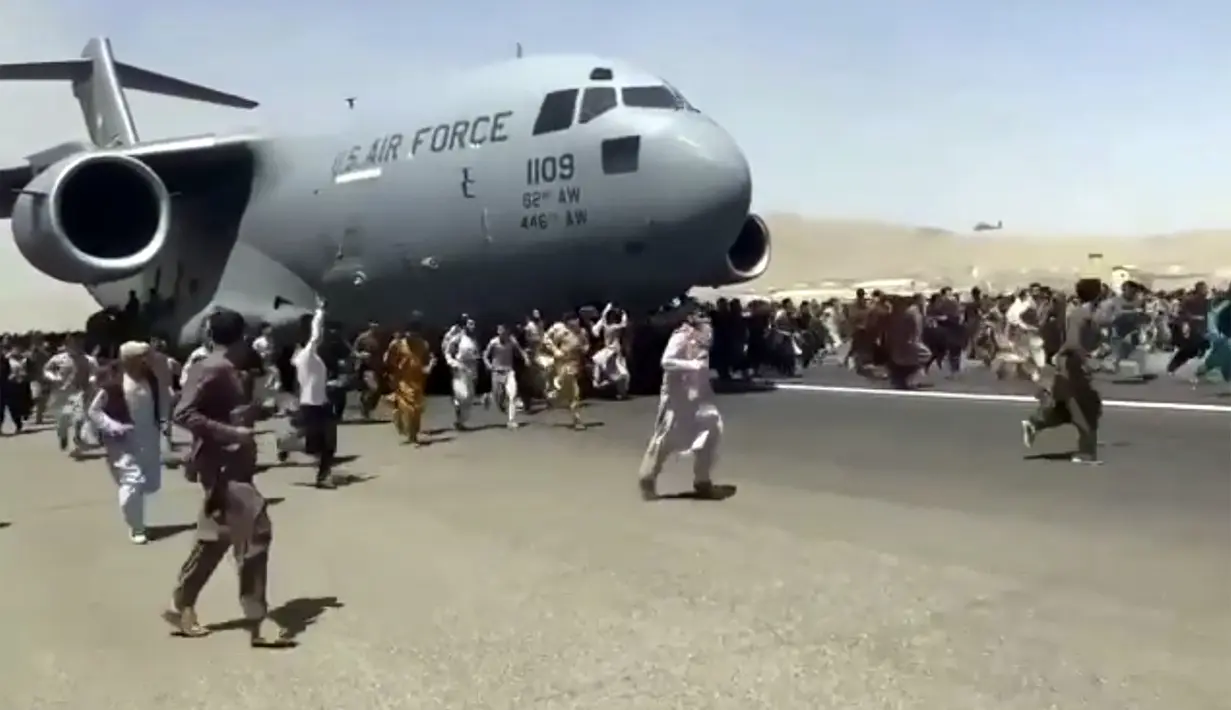 Ratusan orang berlari di samping pesawat angkut C-17 Angkatan Udara AS di landasan bandara internasional, di Kabul, Afghanistan (16/8/2021).  Ratusan warga Afghanistan berusaha kabur dari negaranya. Hal ini terjadi usai pemberontak Taliban menduduki ibu kota Afghanistan. (Verified UGC via AP)