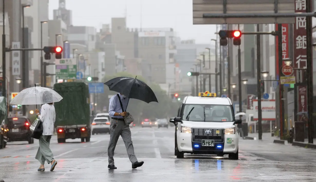 Seseorang berjalan di tengah hujan di depan sebuah stasiun di Shizuoka, sebelah barat Tokyo, Sabtu (13/8/2022). Badai Tropis Meari mengeluarkan hujan lebat di barat daya Jepang saat menuju ke utara menuju ibu kota Tokyo, menurut pejabat cuaca Jepang. (Kyodo News via AP)