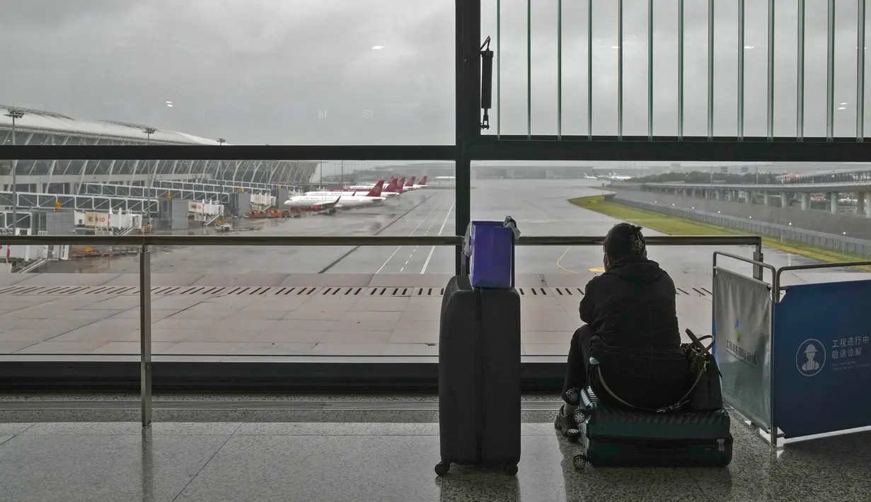 Seorang calon penumpang duduk di kopernya mengamati pesawat yang diparkir di landasan setelah semua penerbangan dibatalkan di Bandara Internasional Pudong, Shanghai, Minggu (25/7/2021). Ratusan jadwal penerbangan dibatalkan saat topan In-Fa bergerak menuju mendarat. (AP Photo/Andy Wong)