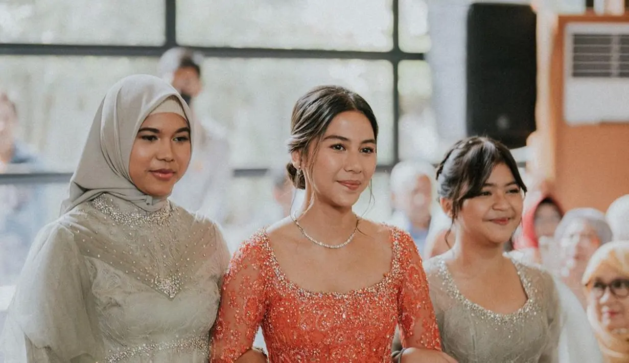 Setelah Raka tiba di tempat acara lamaran, Adinda Thomas pun muncul dengan wajah sumringah dengan kebaya modern warna peach sangat mewah dengan sentuhan payet dan swarovski. Untuk polesan makeup-nya, pemain film KKN Desa Penari itu memilih warna natural dan nude. Kalung simpel yang dipakainya mendukung penampilannya jadi makin cantik dan elegan. (Liputan6.com/IG/@adindathomas)