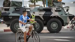 Seorang anak mengendarai sepeda saat tentara Maroko berpatroli di tengah wabah baru virus corona baru di kota Tangiers (11/8/2020). Tentara dikerahkan untuk meredam Lonjakan kasus Covid-19 di negara tersebut. (AFP/Fadel Senna)