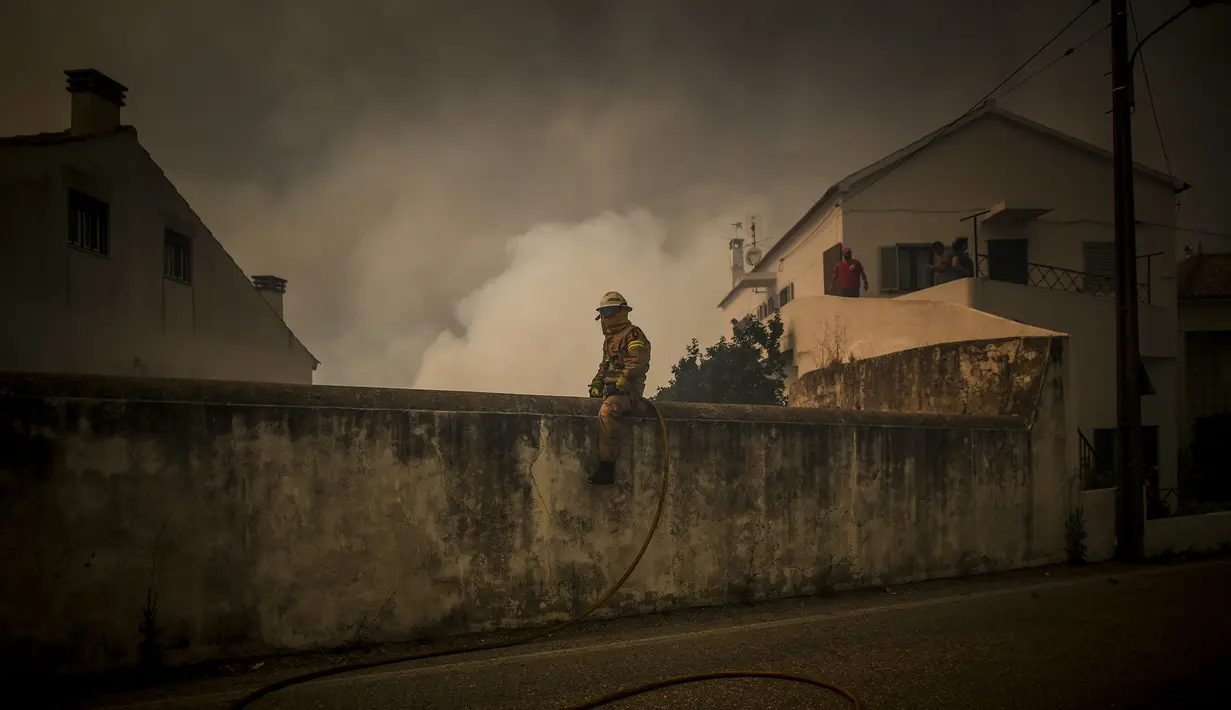 Seorang Pemadam Kebakaran duduk di atas tembok ketika api  mendekati desa Cardigos di Macao, Portugal tengah (21/7/2019).  Kebakaran hutan tersebut memaksa penduduk desa dievakuasi ketempat yang lebih aman. (AFP Photo/Patricia De Melo Moreira)