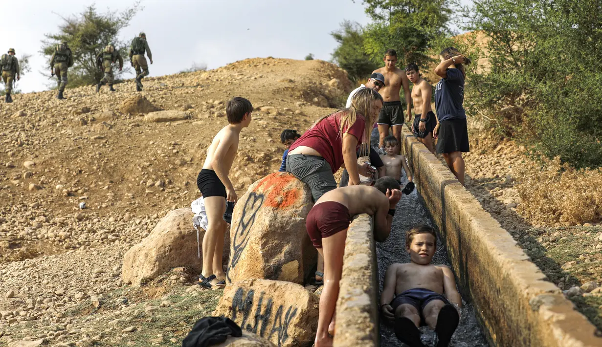 Anak-anak Israel bermain air di sebuah kanal kecil di Desa Al-Auja selama perayaan keagamaan Yahudi dalam Festival Sukkot di Tepi Barat (17/10/2019). Festival Yahudi di Sukkot memperingati pengembaraan padang pasir alkitabiah orang Israel setelah eksodus mereka dari Mesir. (AFP Photo/Menahem Kahana)