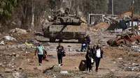 Warga Palestina yang melarikan diri dari utara melalui jalan Salaheddine di distrik Zeitoun di pinggiran selatan Kota Gaza berjalan melewati tank-tank tentara Israel pada 24 November 2023 setelah gencatan senjata selama empat hari yang dimulai sejak pagi hari. (MAHMUD HAMS/AFP)