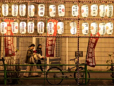 Orang-orang berjalan melewati lentera kertas pada pekan raya akhir tahun di Distrik Nihonbashi, Tokyo, Jepang, 26 Desember 2022. Tak hanya menyuguhkan pemandangan indah dan makanan yang lezat, Jepang juga menjadi negara yang tepat untuk merayakan tahun baru. (Yuichi YAMAZAKI/AFP)