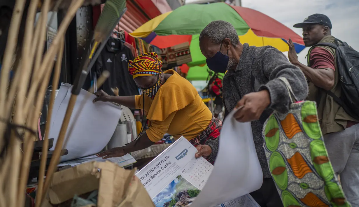 Pasangan bertopeng memilah barang di pasar outdoor dekat pangkalan taksi Baragwanath di Soweto, Afrika Selatan, Kamis (2/12/2021). Afrika Selatan mempercepat kampanye vaksinasi untuk memerangi lonjakan pesat kasus Covid-19 usai mendeteksi varian Omicron pekan lalu. (AP Photo/Jerome Delay)