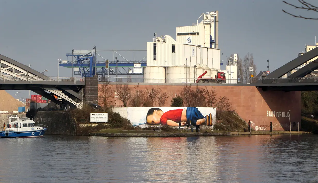 Sebuah grafiti raksasa bergambar balita Aylan Kurdi yang meninggal karena tenggelam, di dinding pinggiran sungai di Frankurt, Jerman, 10 Maret 2016. Gambar tersebut dibuat untuk menarik simpati pengendara, wisatawan dan dunia.  (Daniel ROLAND/AFP)