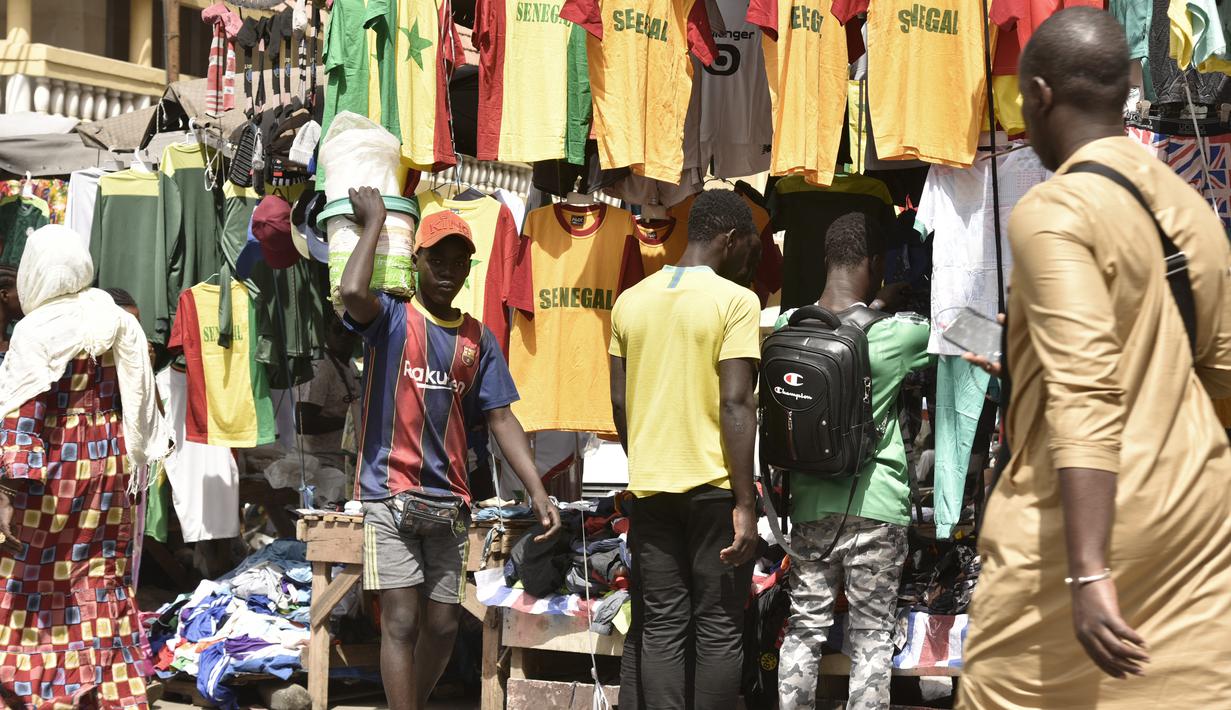 Seorang pria berjalan melewati kios yang menjual kaus tim sepak bola Senegal di Dakar (4/2/2022). Senegal akan bertanding melawan Mesir pada babak final Piala Afrika 2021 di Paul Biya stadium, Senin (7/2/2022) dini hari WIB besok. (AFP/Seyllou)