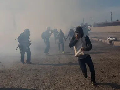 Imigran menghindari gas air mata petugas patroli perbatasan AS di dekat pagar pembatas antara Meksiko dan Amerika Serikat di Tijuana, Meksiko (25/11). Walikota Tijuana telah menyatakan krisis kemanusiaan di kota perbatasannya. (AP Photo/Rodrigo Abd)