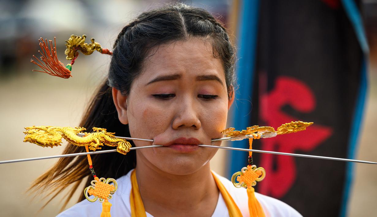 Seorang wanita menusuk pipinya dengan besi  saat mengikuti prosesi perayaan Festival Vegetarian tahunan di Phuket, Thailand, Kamis (3/10/2019). Festival menyiksa diri ini dipercaya bagi warga Phuket akan mendapat kesehatan dan ketenangan pikiran. (AFP Photo/Mladen Antonov)