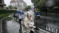 Pejalan kaki dan seorang pengendara sepeda motor menggunakan perlengkapan hujan saat cuaca buruk akibat Topan Bebinca di Shanghai pada Senin 16 September 2024. (Hector RETAMAL/AFP)