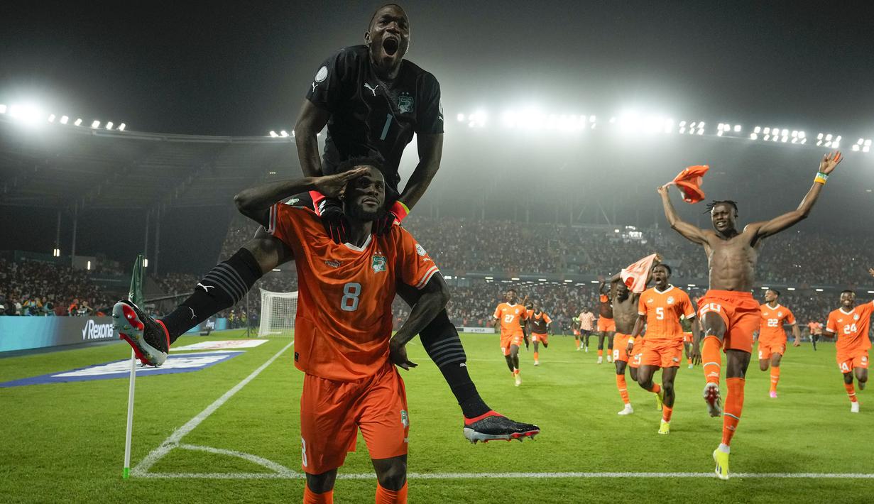 Pemain Pantai Gading, Franck Kessie (bawah) dan kiper Yahia Fofana merayakan kemenangan atas Senegal pada babak 16 besar Piala Afrika 2023 di Stade Charles Konan Banny, Yamoussoukro, Selasa (30/01/2024) dini hari WIB. Pantai Gading menang dengan skor 5-4 pada babak adu penalti. (AP Photo/Themba Hadebe)