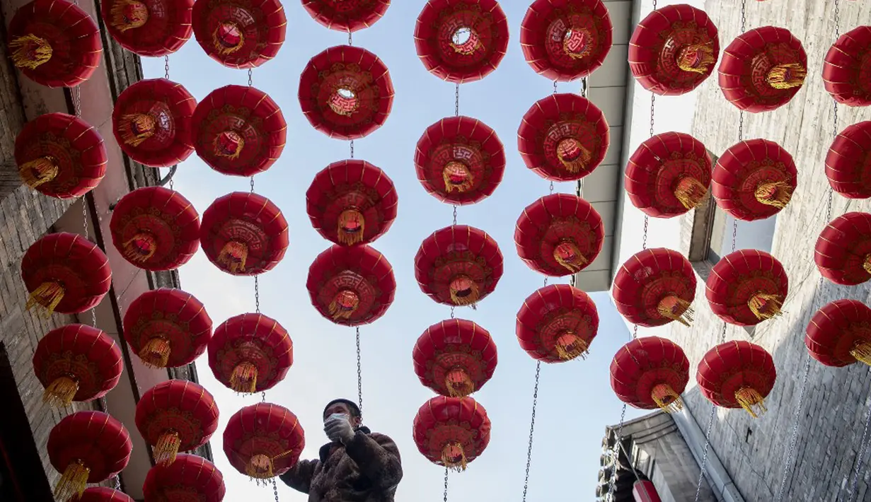 Seorang pekerja memasang lentera tradisional Tiongkok di sepanjang gang menjelang Tahun Baru Imlek di Beijing, China, 2 Februari 2021. Imlek tahun ini jatuh pada tanggal 12 Februari 2021. (NOEL CELIS/AFP)