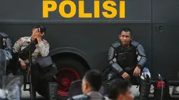 Polisi beristirahat di samping kendaraan taktis di depan Istana Negara, Jakarta, Jumat (4/11). Ribuan aparat gabungan disiagakan saat massa melakukan aksi menuntut penegakan hukum kasus dugaan penistaan agama. (Liputan6.com/Helmi Fithriansyah)