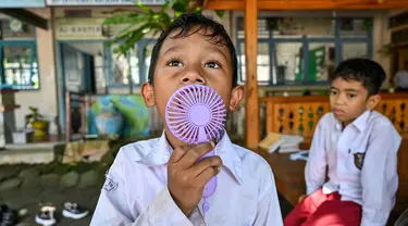 Seorang siswa menggunakan kipas angin portabel saat belajar di luar kelas selama gelombang panas di sebuah sekolah dasar di Banda Aceh pada 7 Mei 2024. (CHAIDEER MAHYUDDIN/AFP)
