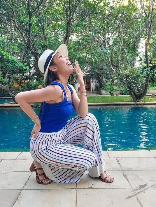 Saat liburan, Ayu Dewi memadukan tank top biru dengan colored stripe pants. Outfit santai ini tampak feminin dengan mengenakan sandal heels berwarna cokelat. (instagram/ayudewi7984)