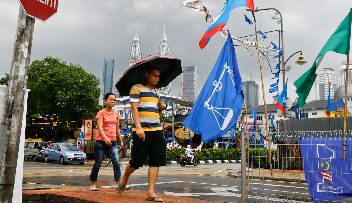 Warga berjalan di samping bendera partai politik dekat Menara Kembar Petronas, Kuala Lumpur, Malaysia, Senin (7/5). Malaysia akan melangsungkan pemilu pada 9 Mei 2018. (AP Photo/Aaron Favila)