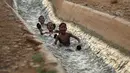 Anak-anak bermain di aliran mata air yang digunakan untuk irigasi untuk mendinginkan tubuh saat suhu udara mencapai 44 derajat Celcius di kota Jericho, Tepi Barat (1/9/2020). (AFP Photo/Ahmad Gharabli)
