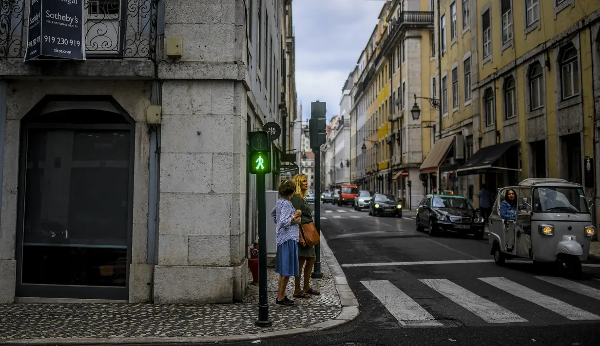 Dua orang menunggu untuk menyeberang jalan di pusat kota Lisbon, Portugal, Senin (13/9/2021). Portugal hari ini mengakhiri aturan wajib penggunaan masker di jalan-jalan. (PATRICIA DE MELO MOREIRA / AFP)