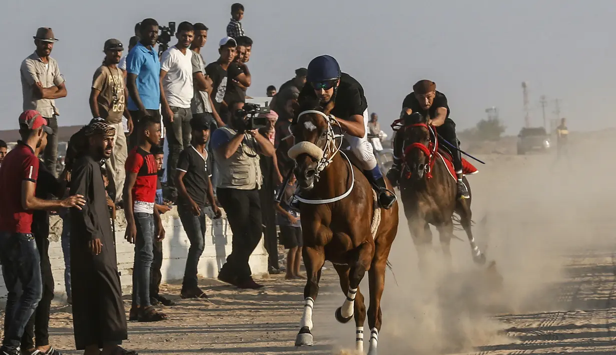 Warga menyaksikan para joki memacu kudanya saat bersaing dalam balap kuda di Rafah, Jalur Gaza, Palestina, Selasa (10/9/2019). Balapan kuda tradisional Palestina tersebut digelar di bekas lokasi bandara Jalur Gaza yang telah hancur. (AFP Photo/Said Khatib)