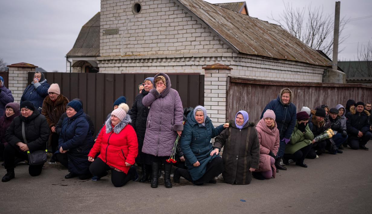 Para pelayat berlutut menunggu peti mati Oleksandr Maksymenko (38) lewat saat pemakamannya di kampung halamannya di Kniazhychi, sebelah timur Kyiv, Ukraina, 13 Februari 2023. Oleksandr Maksymenko, seorang warga sipil yang menjadi sukarelawan di angkatan bersenjata Ukraina, tewas dalam pertempuran di daerah Bakhmut. (AP Photo/Emilio Morenatti)