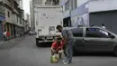 Para pria menyedot bensin mobil yang akan mereka simpan dan kemudian kembali ke pompa bensin untuk diisi lagi, di lingkungan San Juan di Caracas (19/1/2021). SPBU hanya akan mengisi tangki mobil dan motor, tetapi tidak untuk wadah agar orang tidak menyimpan bensin. (AP Photo/Matias Delacroix)