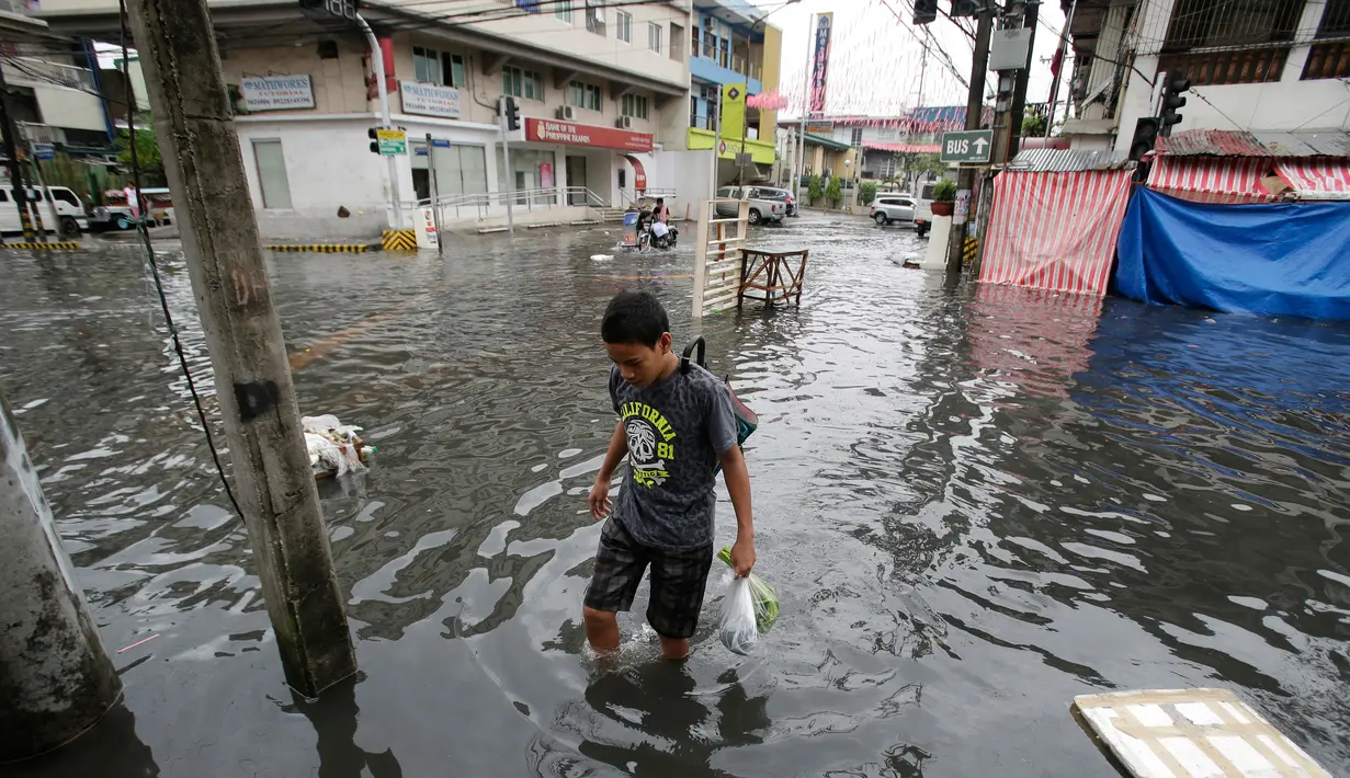 Warga berjalan ditengah banjir usai topan Nock-Ten menerjang kota Quezon, utara Manila, Filipina, (26/12). Topan super Nock-ten atau dikenal dengan Nina menerjang Filipina bertepatan saat Natal. (AP Photo / Aaron Favila)