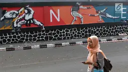 Mahasiswa melintas di depan mural bertema Asian Games 2018 di kawasan Universitas Negeri Jakarta, Kamis (16/8). Mural karya mahasiswa seni rupa tersebut dibuat dalam rangka menyambut Asian Games 2018. (Liputan6.com/Immanuel Antonius)