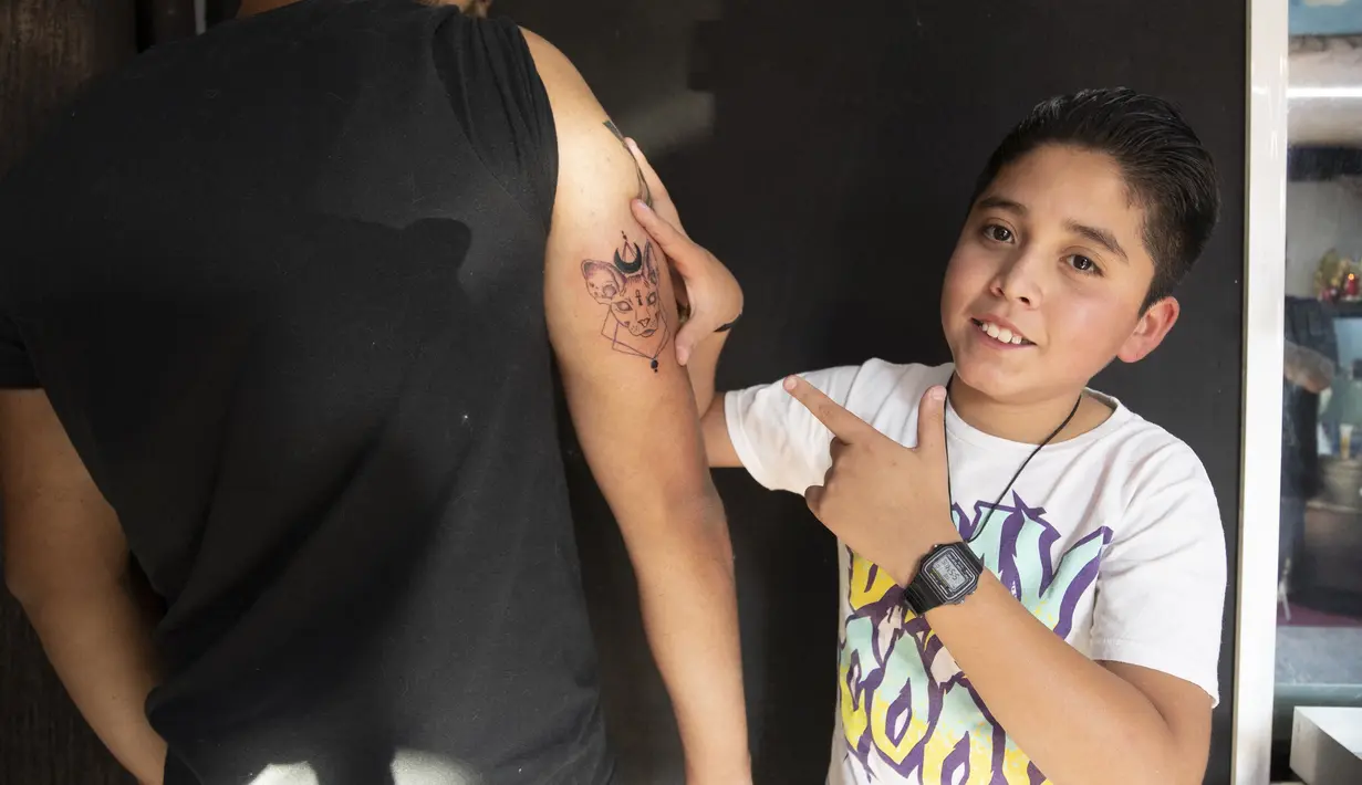 Brandon Burgos berpose setelah menato seseorang di kota Puebla, Meksiko, pada 10 November 2021. Brandon Burgos dengan hati-hati menggunakan mesin tato di studio ayahnya. Dia baru berusia 11 tahun, tetapi anak sekolah itu sudah memiliki sekitar 30 tato atas namanya. (JUAN CARLOS SANCHEZ/AFP)