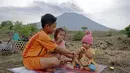 Anak-anak duduk di areal perkebunan dengan latar belakang Gunung Agung di Karangasem, Bali, Rabu (29/11). Meskipun Gunung Agung terus menunjukkan peningkatan aktivitas vulkanik, sebagian warga memilih tetap beraktivitas. (AP/Firdia Lisnawati)