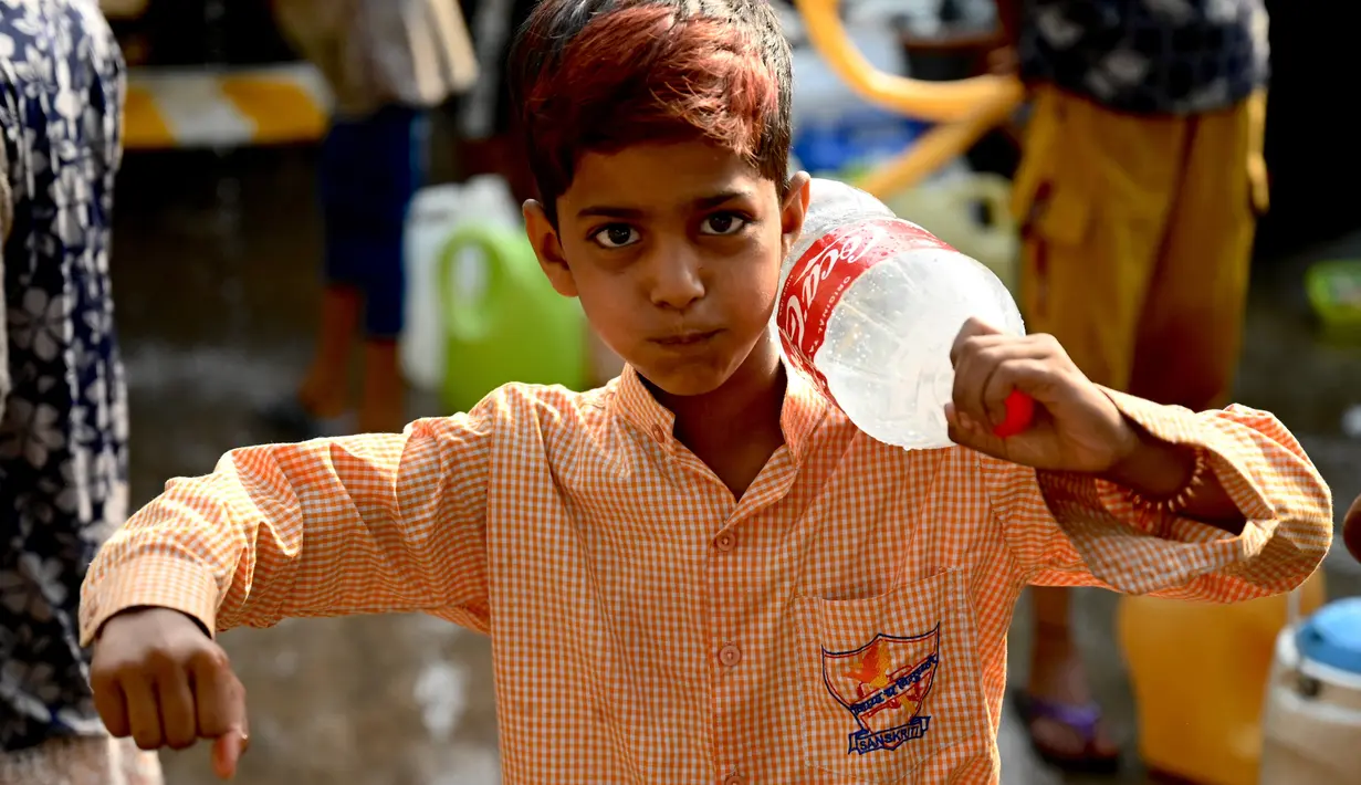 Seorang anak laki-laki bereaksi setelah mengisi botol dengan air dari truk tangki air di lingkungan berpenghasilan rendah di New Delhi pada Kamis (3/6/2021). Kelangkaan air secara tidak proporsional mempengaruhi orang-orang rentan di masyarakat berpenghasilan rendah. (Money SHARMA / AFP)
