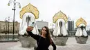 Seorang wanita berselfie di depan "benda seni Matryoshki", tujuh boneka bersarang tradisional Rusia "matryoshka" dengan hiasan kepala "kokoshnik", dengan gedung Pemerintah Rusia terlihat di latar belakang, di pusat kota Moskow (9/9/2021).  (AFP/Kirill Kudryavtsev)