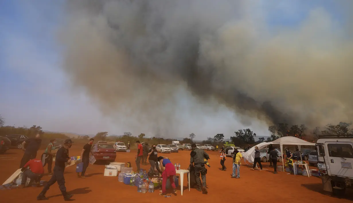 Petugas kepolisian, petugas pemadam kebakaran, dan sukarelawan membawa makanan dan air ke base camp mereka saat api menghanguskan sebagian Taman Juquery di Franco da Rocha, wilayah Sao Paulo, Brasil, Senin (23/8/2021). (AP/Andre Penner)
